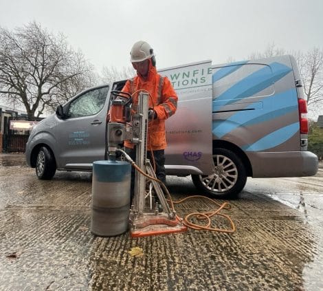 Concrete coring operative drilling a core sample beside Brownfield Solutions van