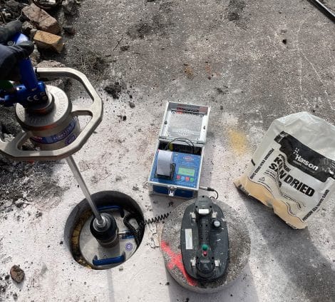 In-situ density testing setup with nuclear density gauge, control unit and sand replacement materials on site.