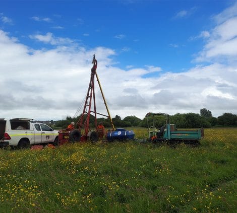 Cable percussion drilling rig and operatives carrying out ground investigation works on a rural site in Poulton.